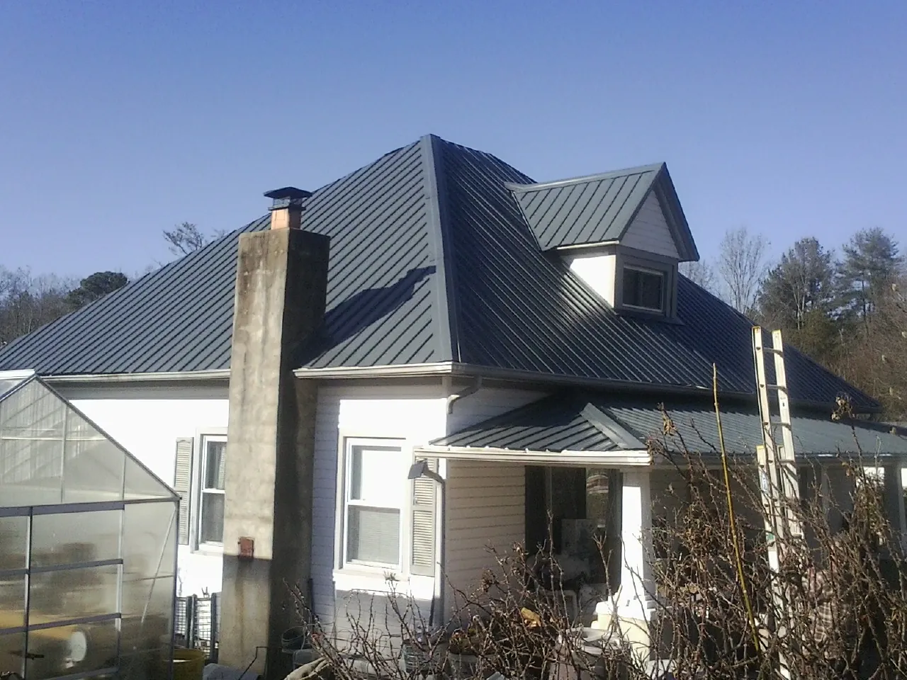 Dark blue standing seam metal roof on a white farmhouse with dormer — Slate & Tile Roof Repair by Roofing Brothers in Elwood